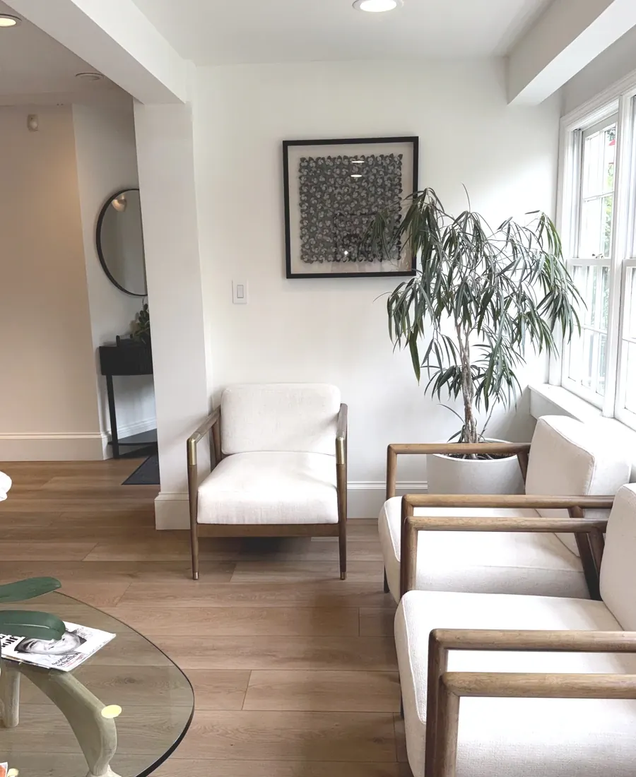 The waiting room, with white armchairs, a glass table and tall windows.